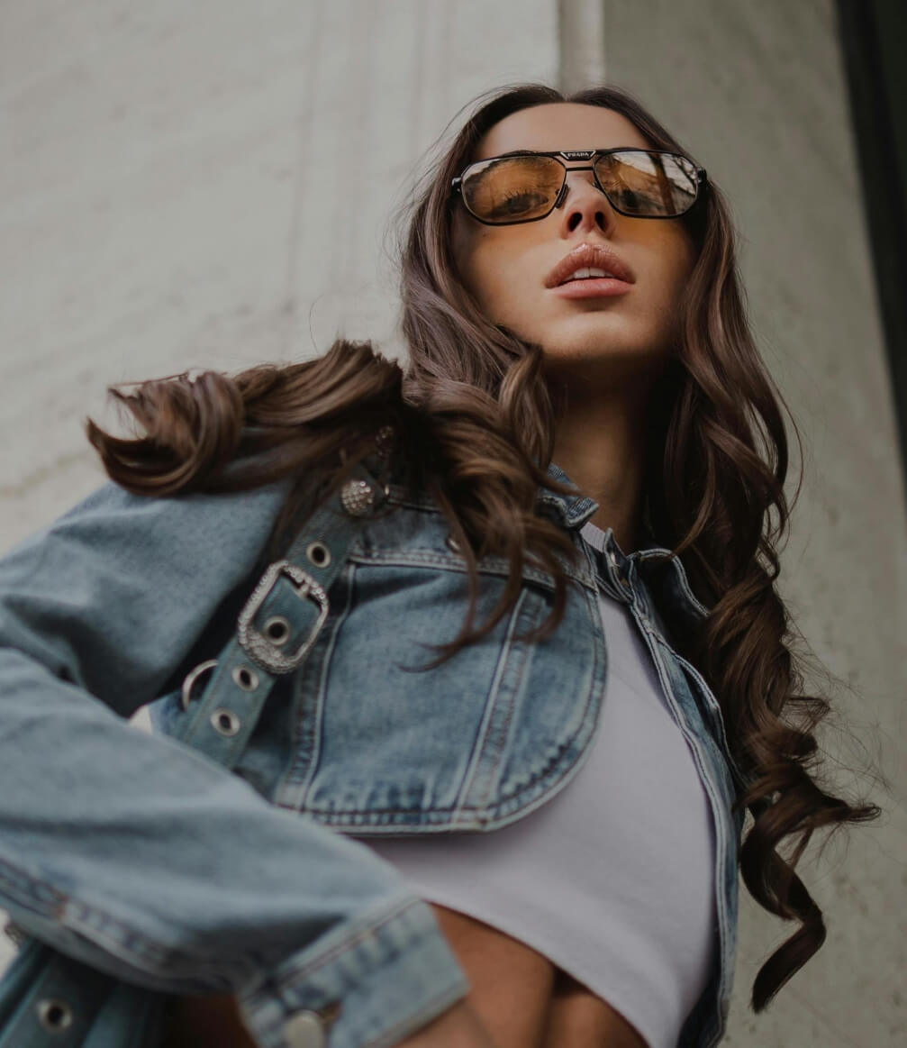 young adult woman wearing cropped denim jacket and sunglasses